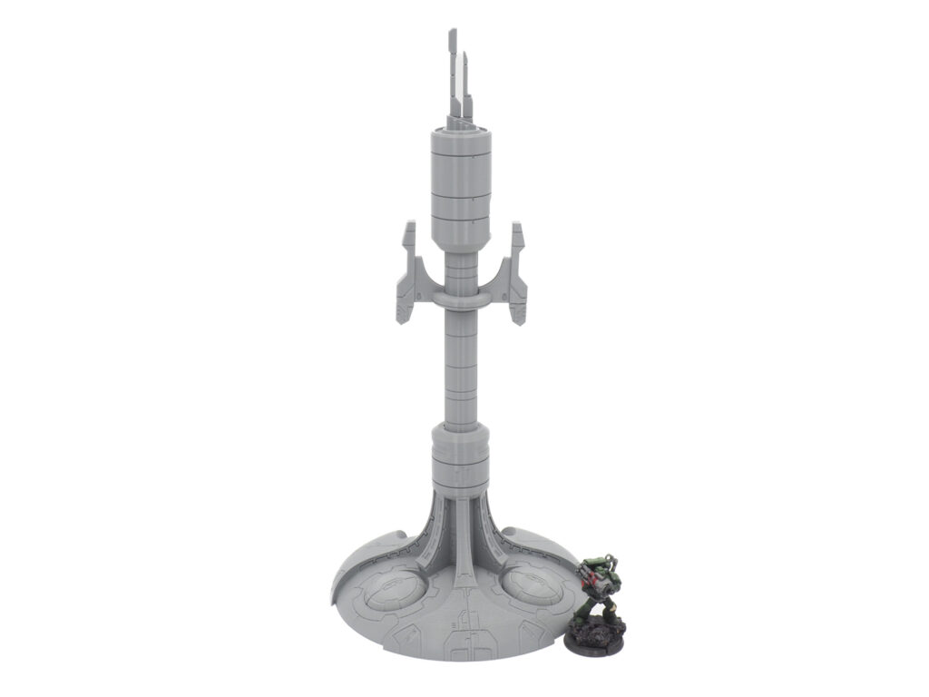 Grey 3D-printed sci-fi antenna tower terrain piece shown next to a painted miniature figure for scale