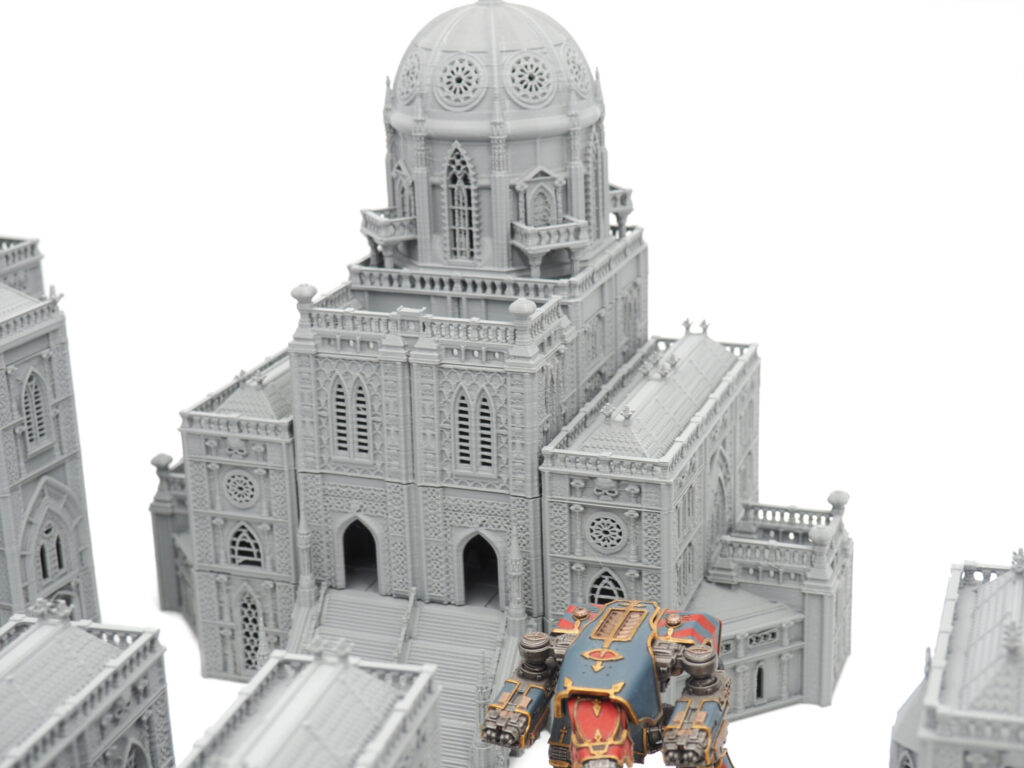 A detailed grey 3D-printed gothic cathedral miniature shown with a painted sci-fi robot for scale