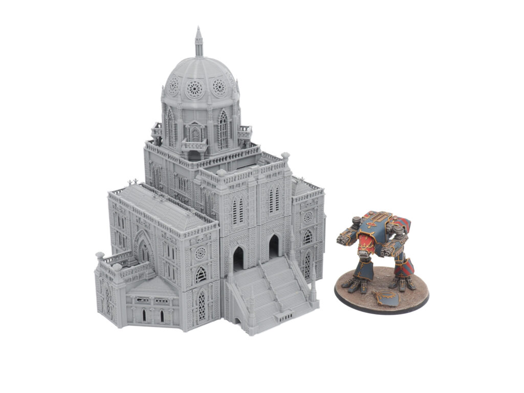 Grey 3D-printed gothic cathedral tabletop terrain model next to a painted miniature for scale