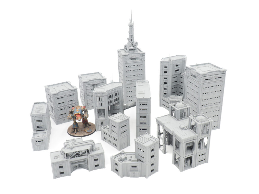 Grey 3D-printed sci-fi miniature buildings for tabletop gaming, shown with a painted mech figure for scale