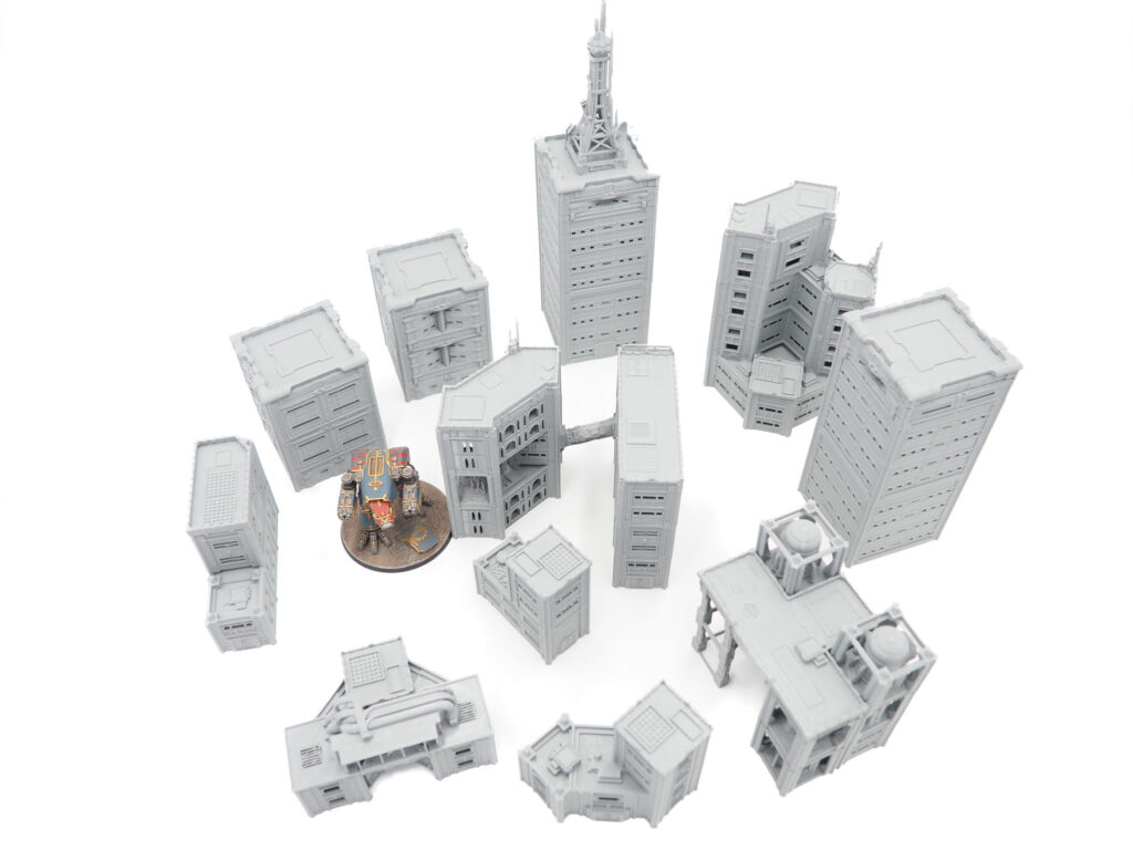 Unpainted grey 3D-printed sci-fi miniature buildings arranged on a white background with a small robot model for scale