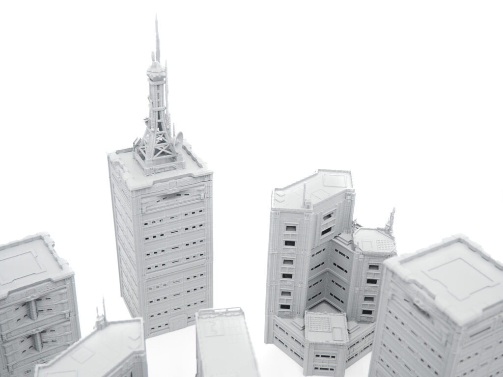 Grey 3D-printed miniature skyscrapers and buildings for tabletop gaming terrain, shot on a white background