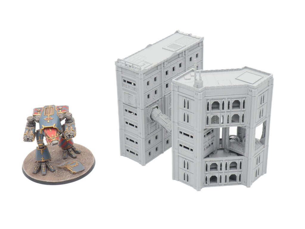 Grey 3D-printed sci-fi buildings connected by a walkway, shown next to a painted miniature mech for scale