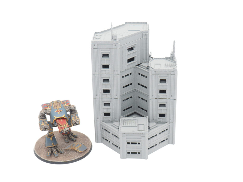 Grey 3D-printed modular sci-fi building terrain next to a painted miniature mech for scale