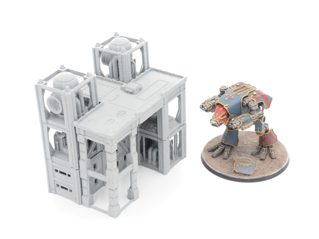 Grey 3D-printed industrial terrain structure next to a painted miniature mech for scale comparison