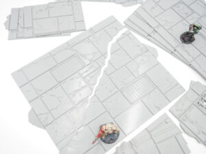 Modular grey 3D-printed floor tiles with cracked details, shown with tabletop miniatures for scale