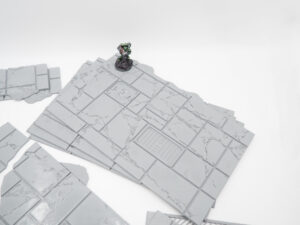 Grey 3D printed modular floor tiles with cracked details, shown with a painted miniature gaming figure for scale