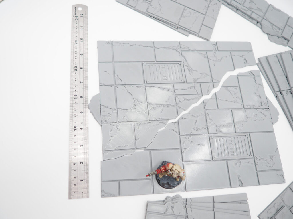 Grey 3D-printed modular stone tiles for tabletop gaming, shown with a ruler and miniature figurine for scale
