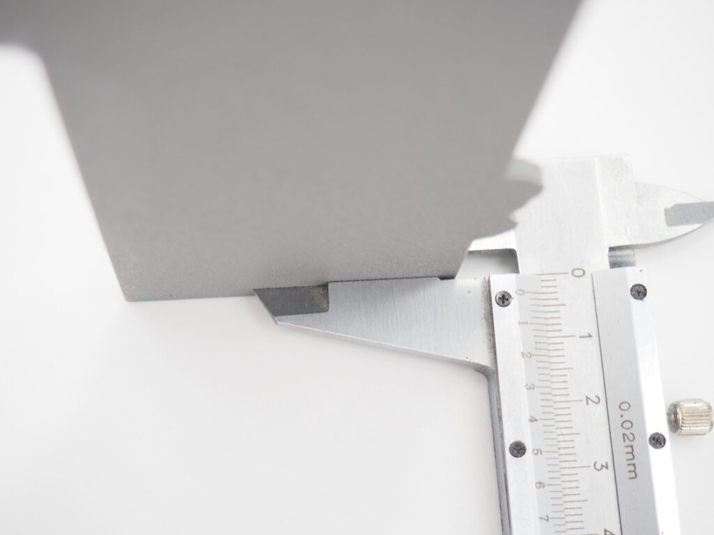 Close-up of a metal caliper measuring a grey 3D printed part to demonstrate dimensional accuracy