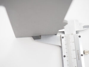 Close-up of a metal caliper measuring a grey 3D printed part to demonstrate dimensional accuracy