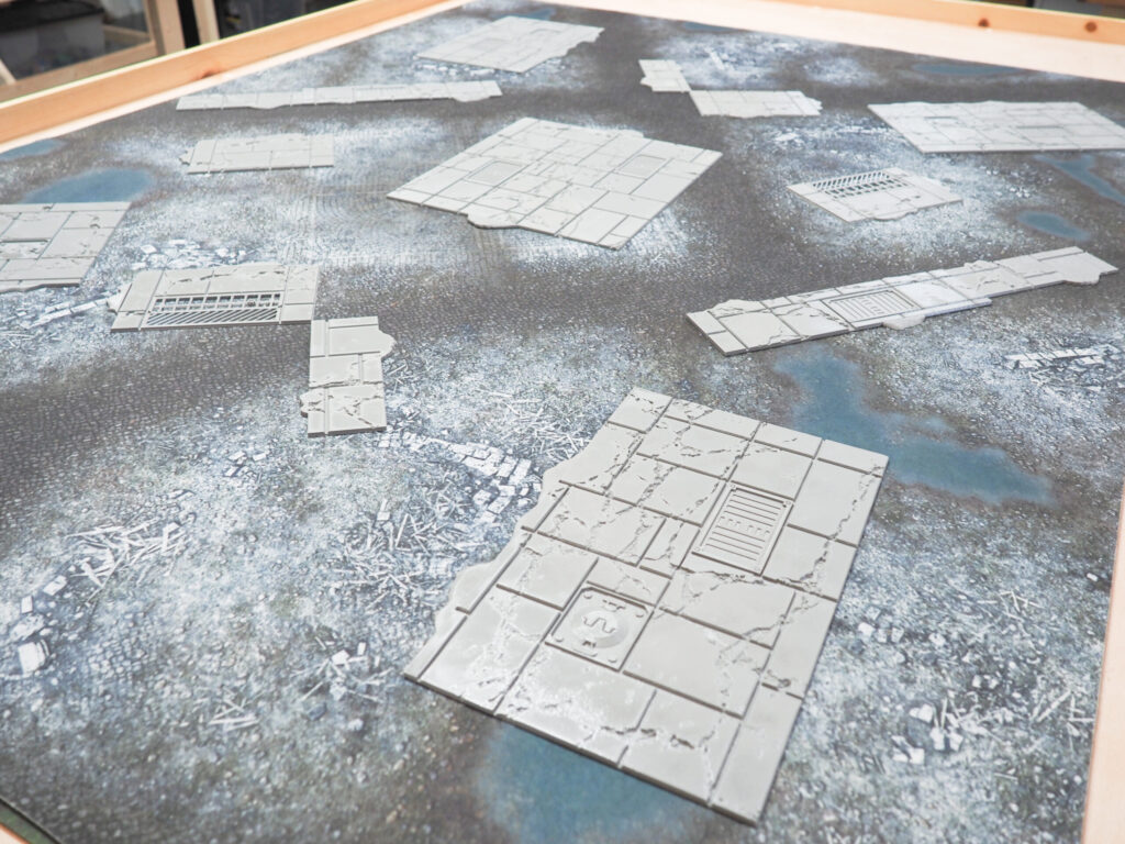 Grey 3D-printed miniature street and ruin tiles for tabletop wargaming, arranged on a textured battle mat