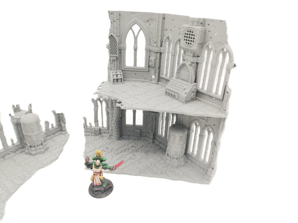 Grey 3D-printed gothic ruin miniature terrain with two levels, shown with a painted figure for scale