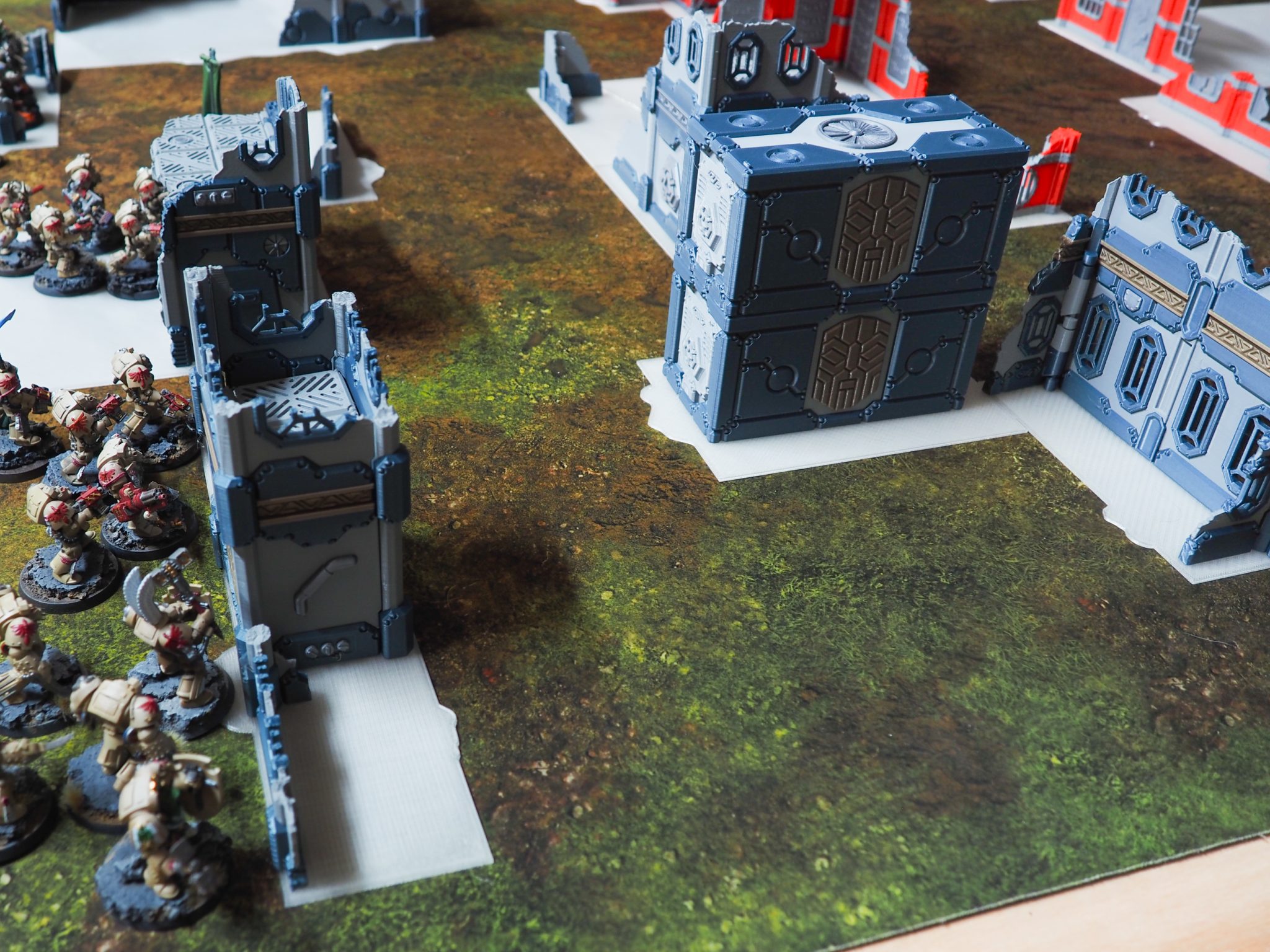 3D-printed modular sci-fi terrain ruins and shipping containers arranged on a wargaming mat beside miniature infantry