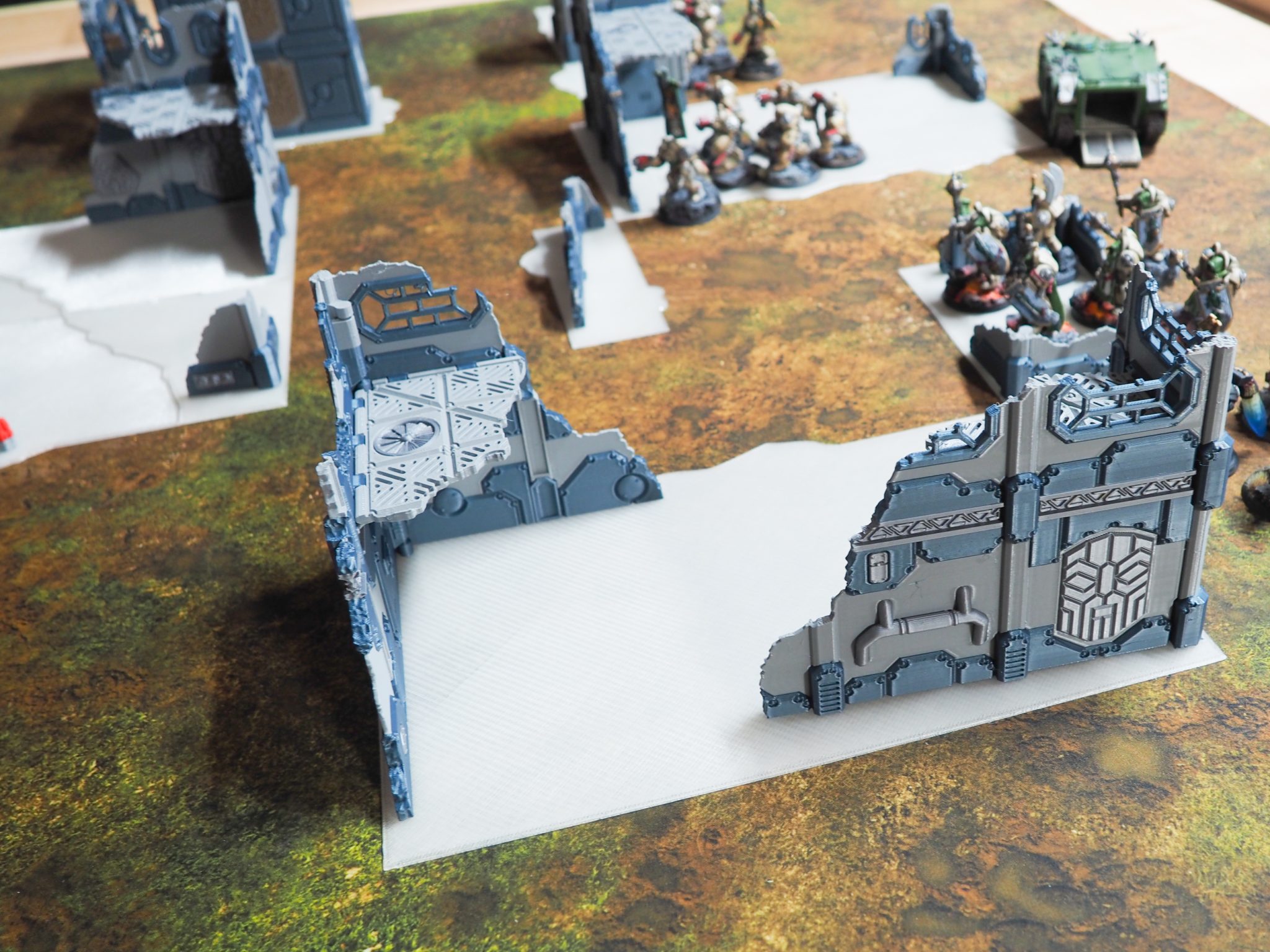 3D-printed sci-fi building ruins and walkways set up on a tabletop gaming mat with miniatures
