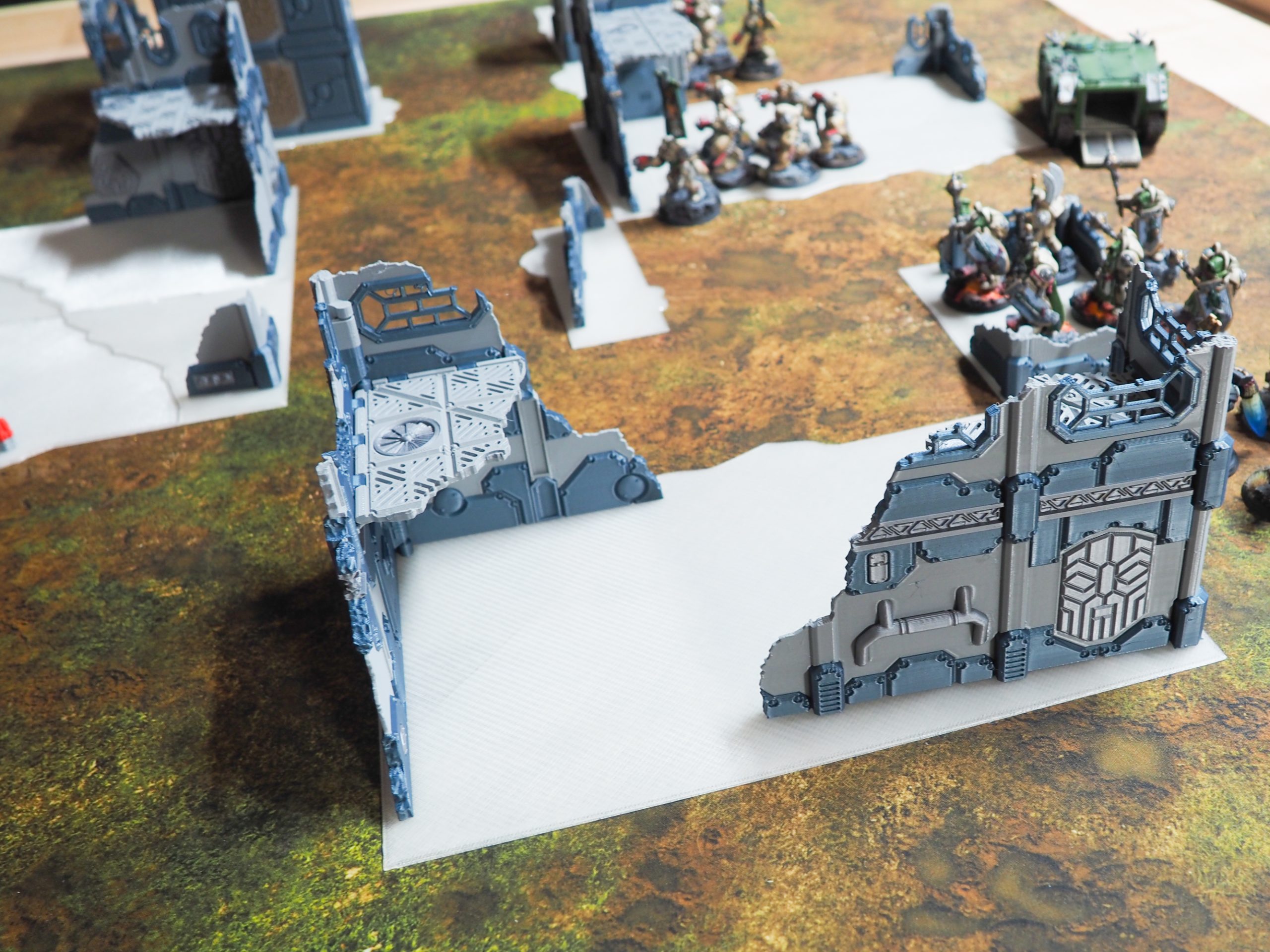 3D-printed sci-fi building ruins and walkways set up on a tabletop gaming mat with miniatures