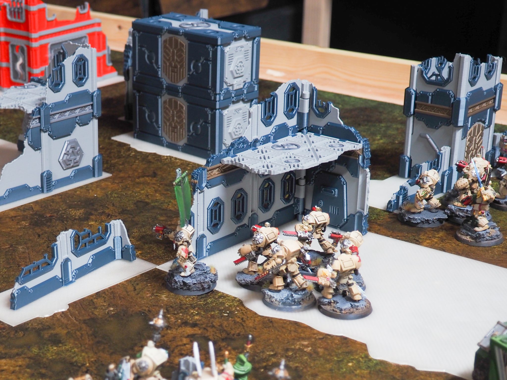 3D-printed sci-fi modular ruined buildings and containers set up on a wargaming table with painted miniatures