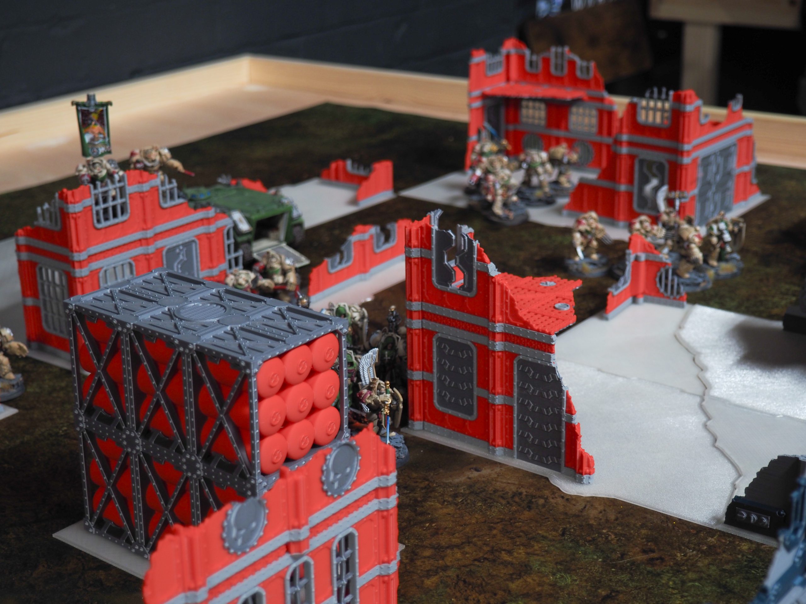3D-printed red and grey industrial ruin and fuel silo terrain on a tabletop wargaming board with miniatures