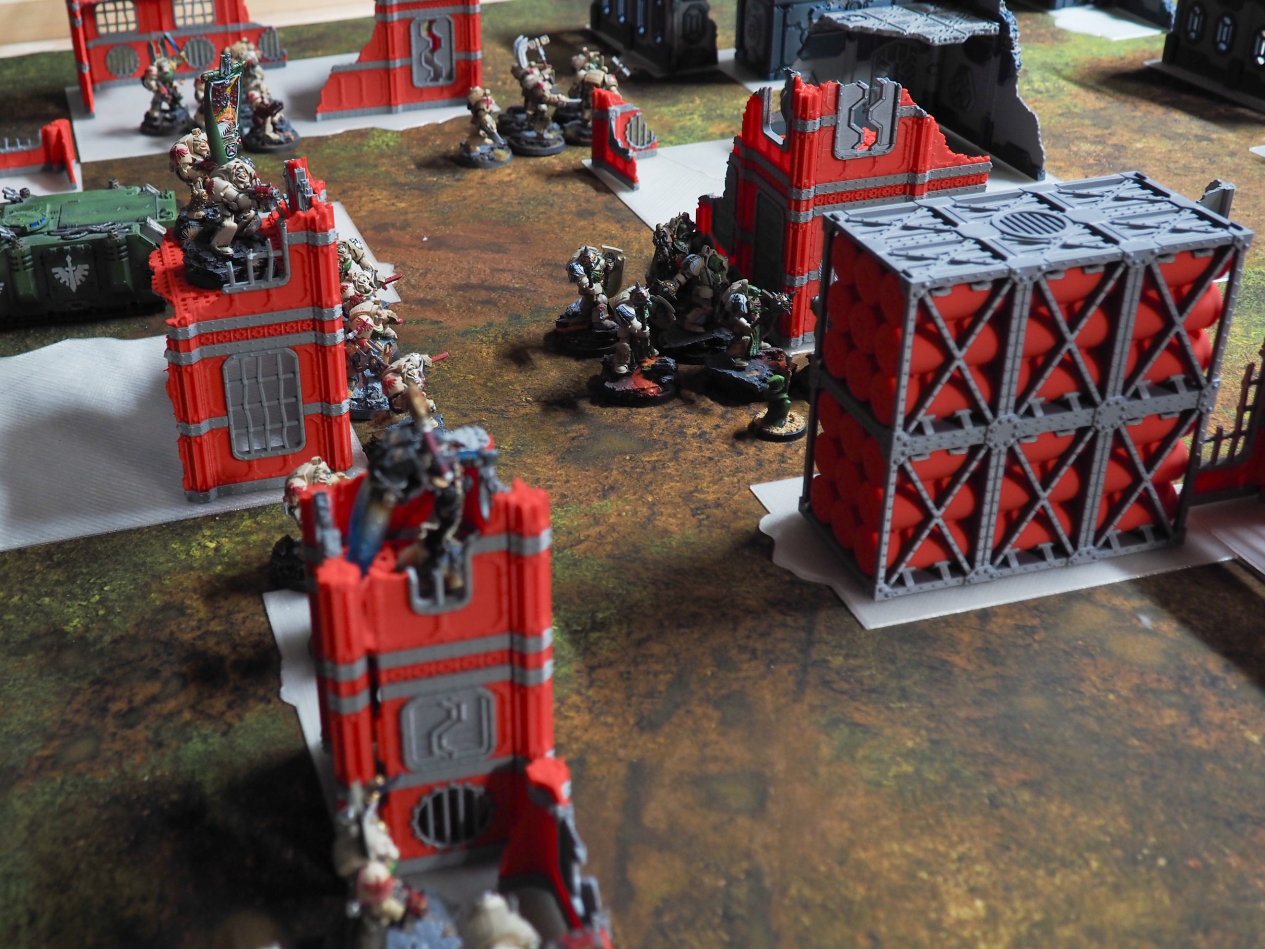 Red and grey 3D-printed sci-fi terrain pieces arranged with miniature figures on a tabletop wargaming mat