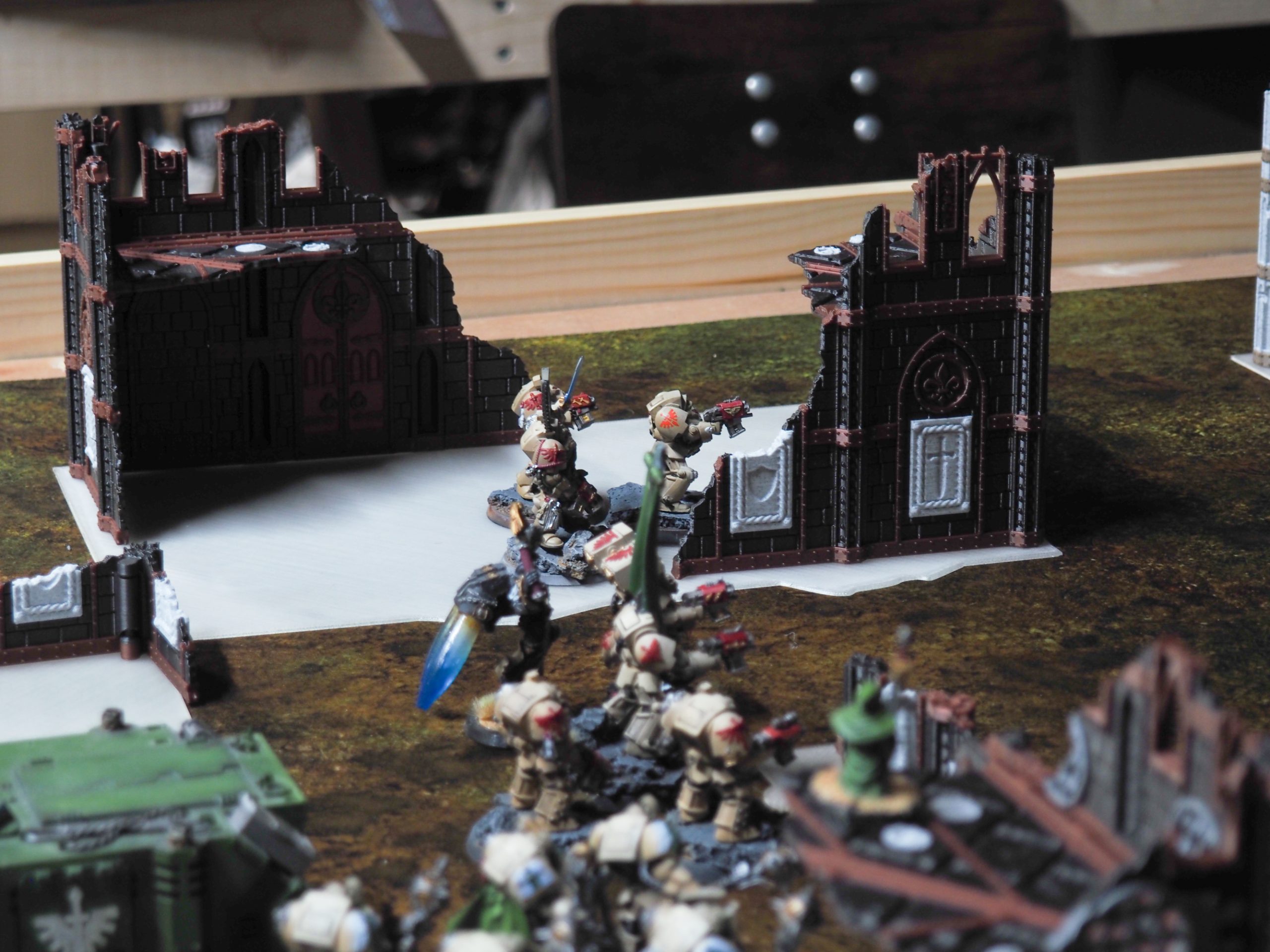 3D-printed gothic ruin terrain pieces set up with painted miniature figures on a tabletop wargaming mat