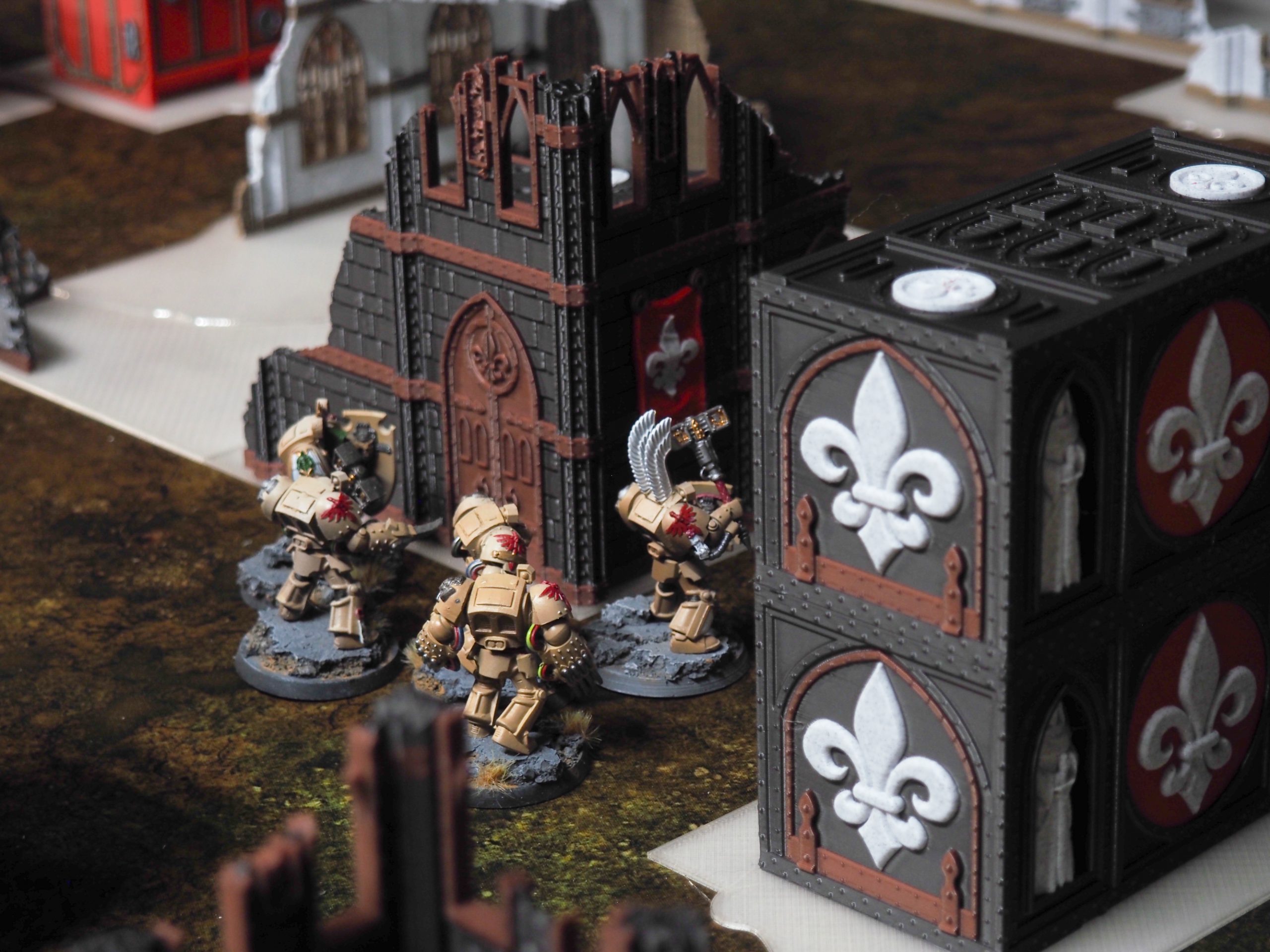 3D-printed gothic ruins and containers with fleur-de-lis motifs displayed with painted wargaming miniatures