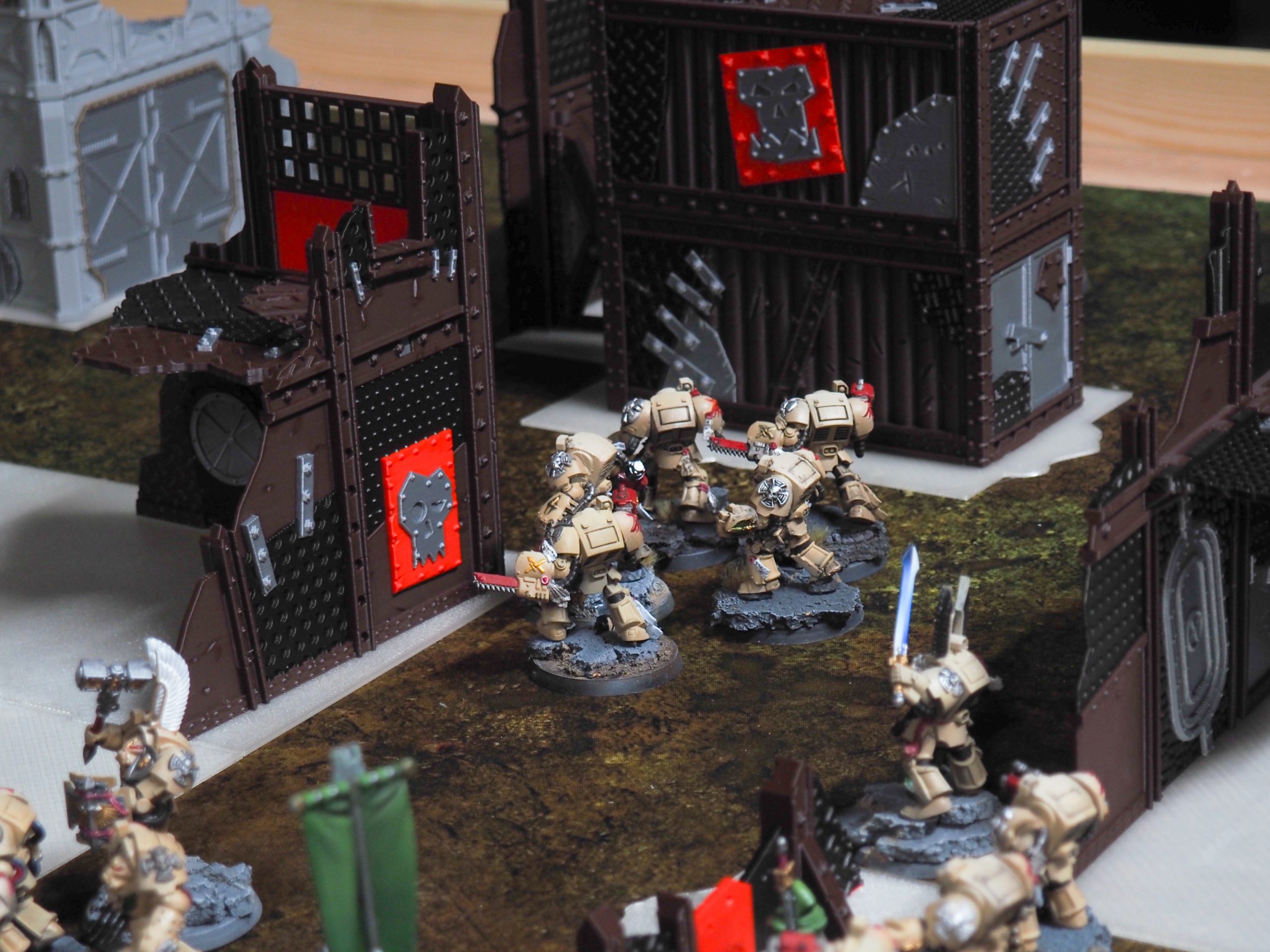Modular 3D-printed industrial wargaming terrain and barricades set up with miniature figures in a tabletop game