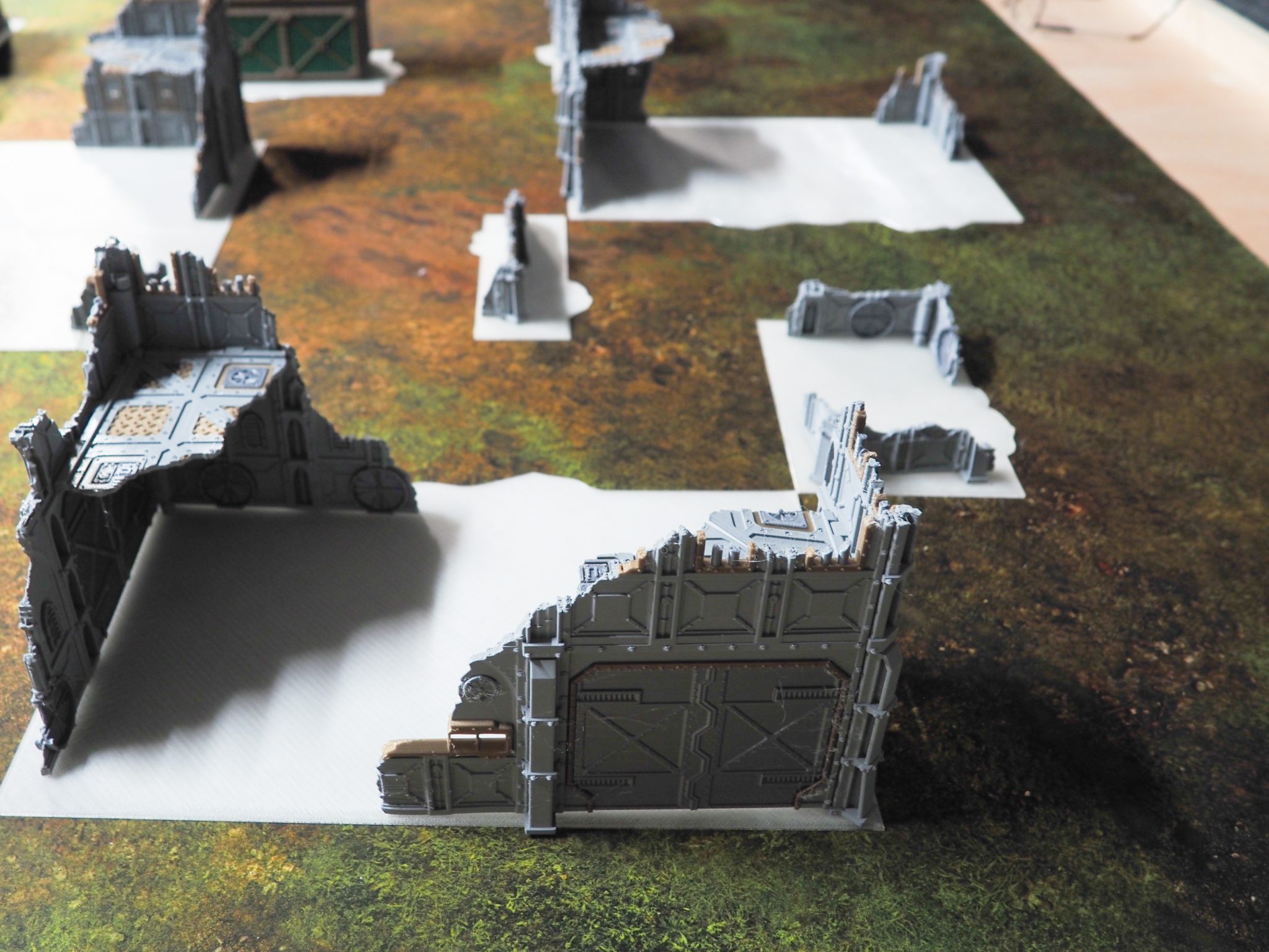 Grey 3D-printed sci-fi ruined building terrain pieces with flat white bases arranged on a tabletop gaming mat