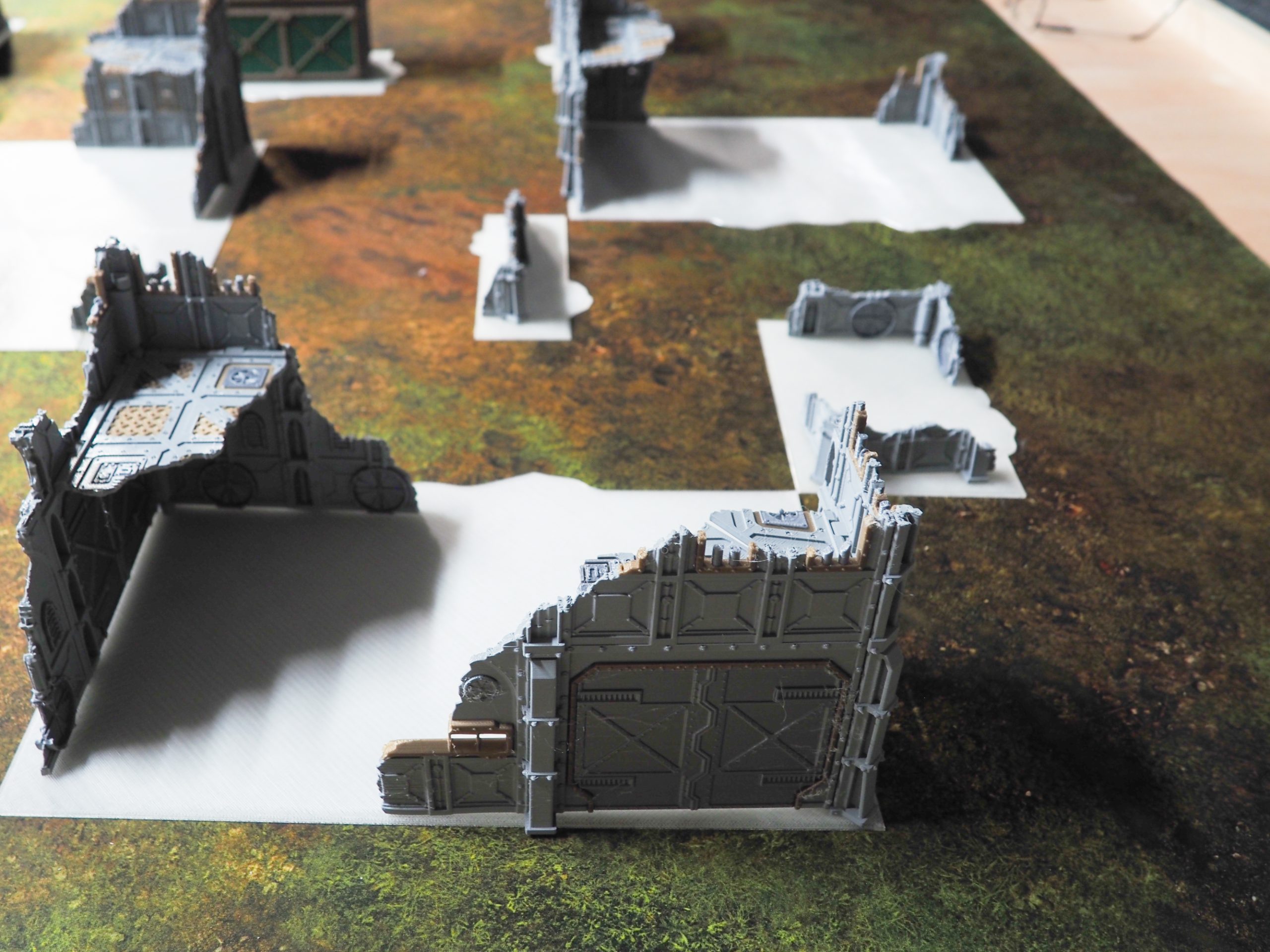 Grey 3D-printed sci-fi ruined building terrain pieces with flat white bases arranged on a tabletop gaming mat