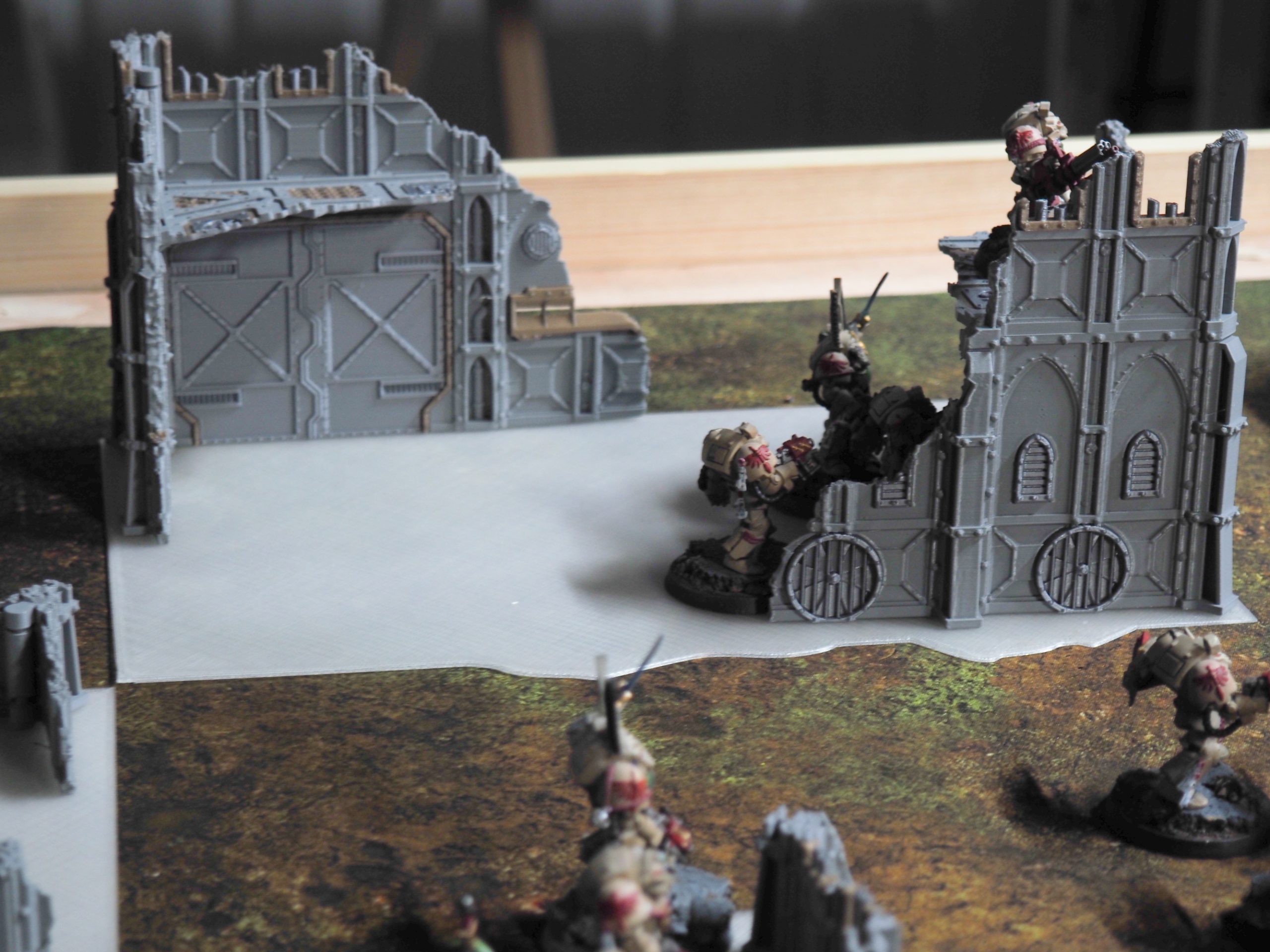 Grey 3D-printed ruined building terrain set up on a gaming mat with painted tabletop miniatures