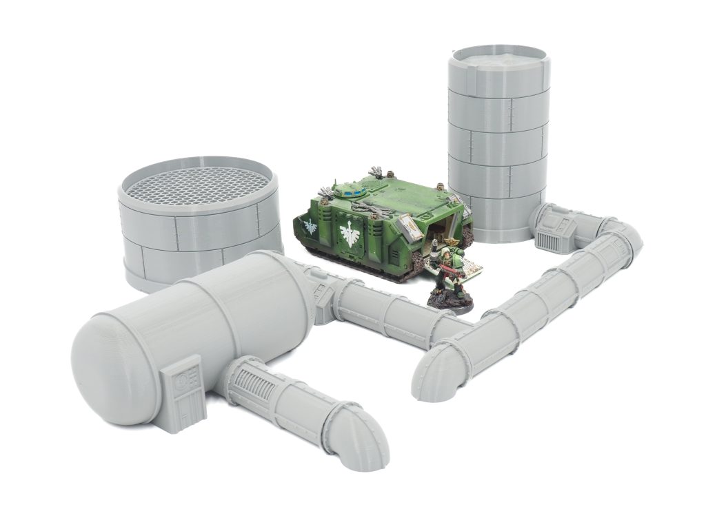 3D-printed grey industrial pipeline and silo terrain set, shown with miniatures for scale