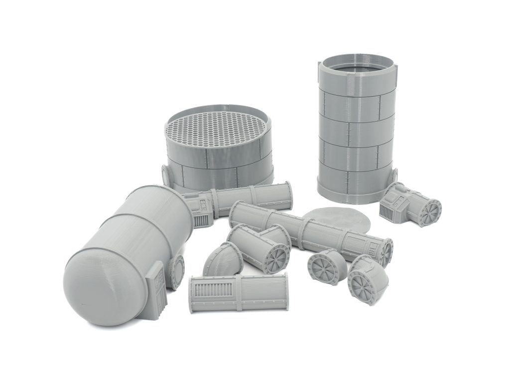 Grey 3D-printed miniature industrial terrain set featuring silos, tanks, and modular pipe sections