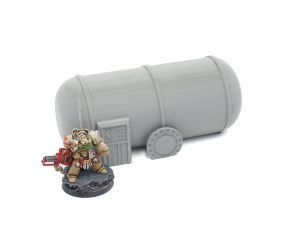 Grey 3D-printed cylindrical storage tank terrain piece shown next to a painted miniature figurine for scale