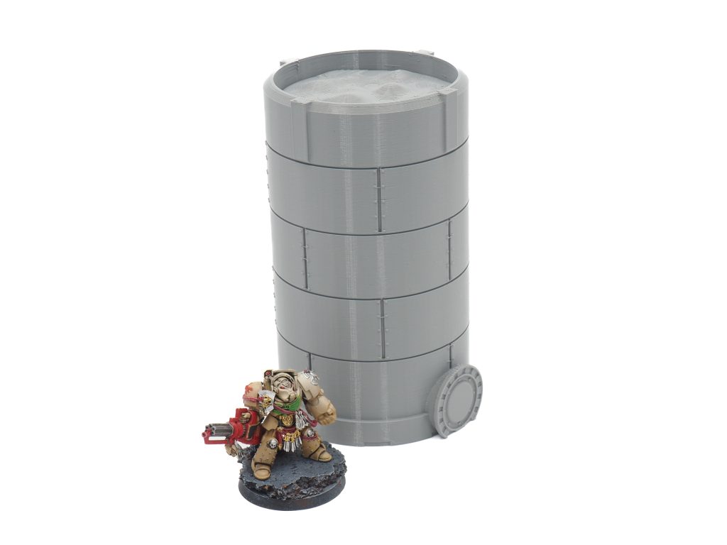 Grey 3D-printed cylindrical storage tank terrain piece next to a painted miniature figurine for scale